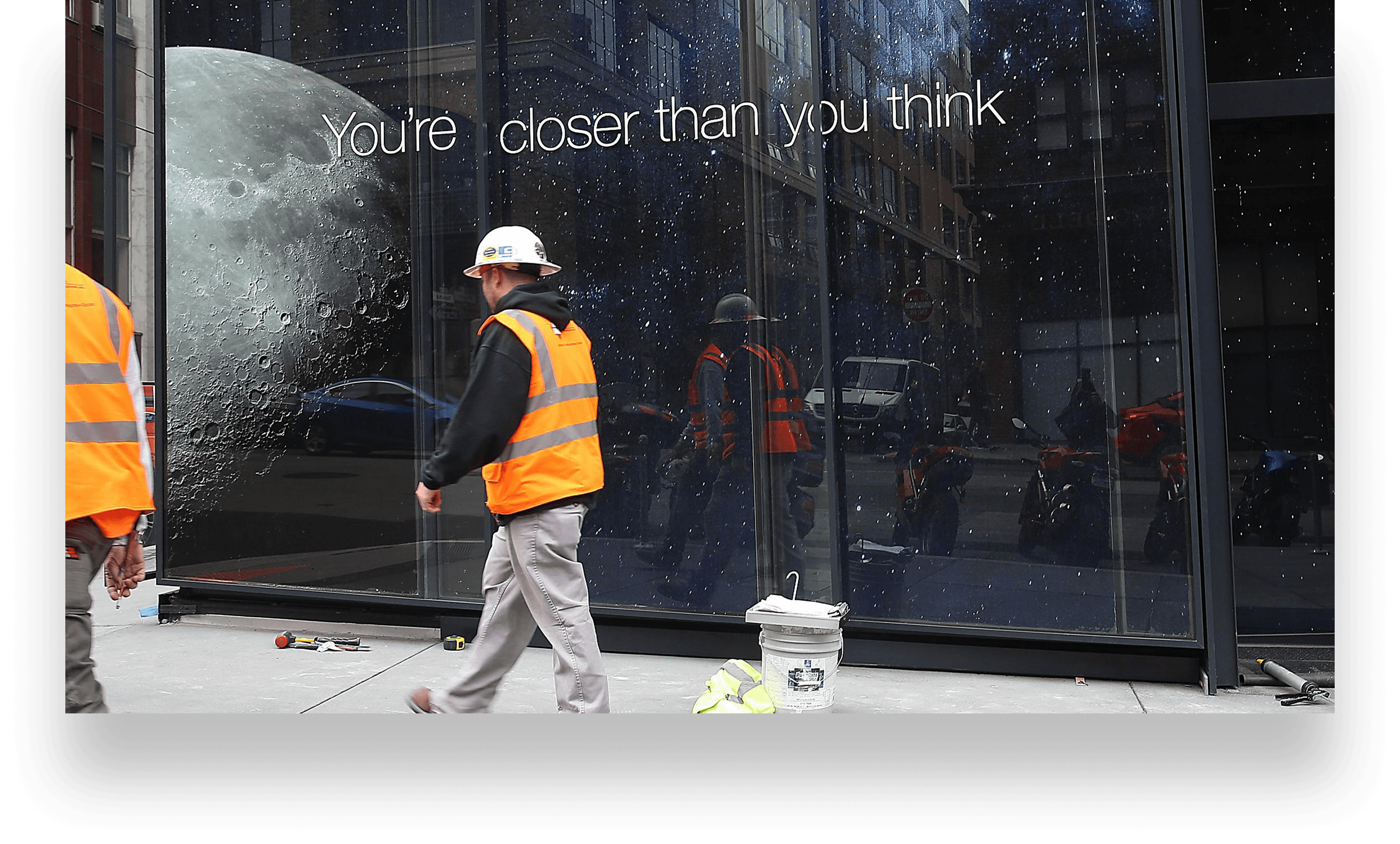 Street-level billboard reading “You’re closer than you think” with the moon, above passers-by on a city sidewalk.